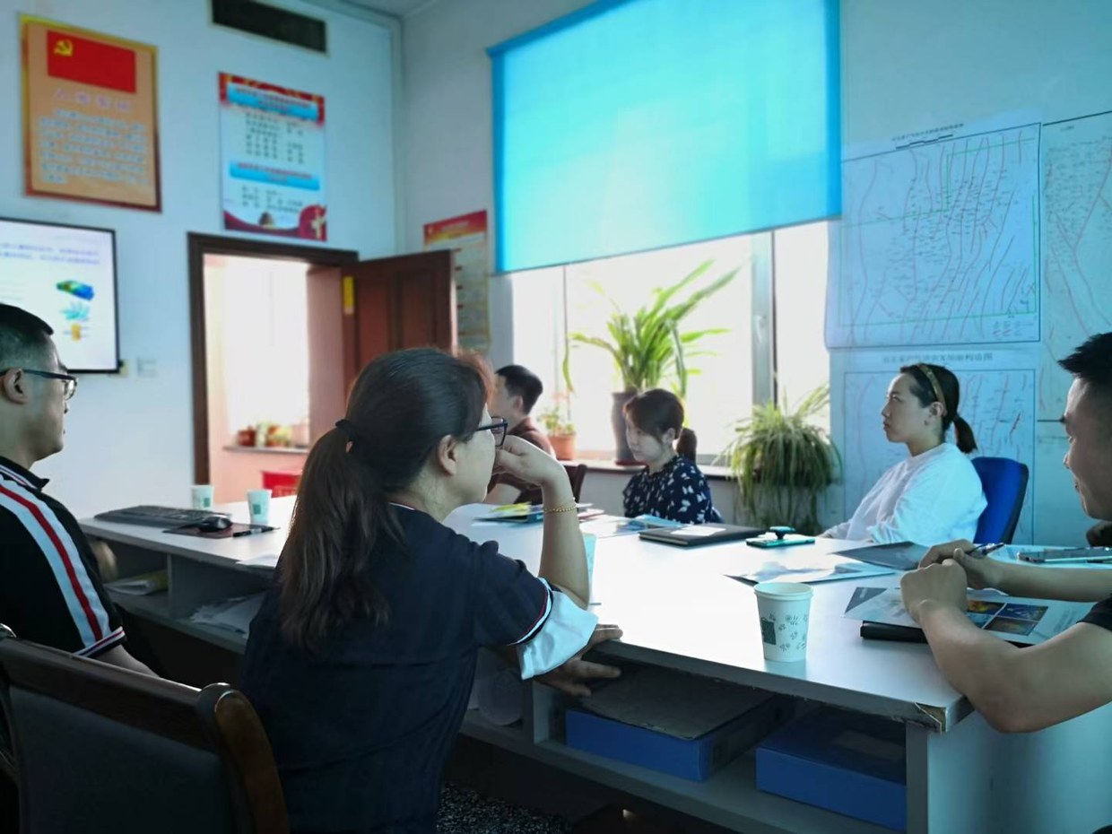 交流现场另一角度，桌上摊着彩色印刷材料，参与者边听边记录