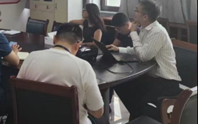 与会人员围坐椭圆会议桌对照电脑屏幕讨论软件使用