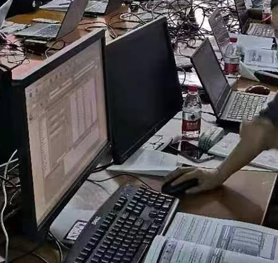 工位上的显示器、键盘与打印资料，屏幕上停留在一份数据表上